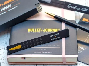 Alle Produkte der Bullet Journal Edition von LEUCHTTURM1917 liegen auf einer hellen Oberfläche verteilt: Bullet Journal, Drehgriffel, Pocket und Pen Loop.