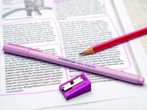 Ein lila Textmarker und Spitzer sowie ein Bleistift von STAEDTLER liegen auf einem Schultext über Hormone. 