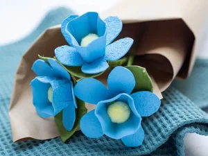 Drei blaue DIY-Blumen aus Eierkartons liegen in Packpapier eingewickelt auf einem grünen Handtuch. Foto: Johanna Rundel