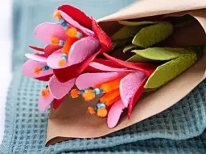 Drei rot-orangene DIY-Blumen aus Eierkartons liegen in Packpapier eingewickelt auf einem grünen Handtuch. Foto: Johanna Rundel