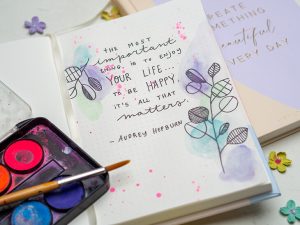 Ein auf geschlagenes Bullet Journal von Rössler, auf dem Deckblatt ist ein Zitat von Audrey Hepburn geschrieben. Der Rest der Seite wurde mit Wasserfarben verschönert. Foto: Johanna Rundel