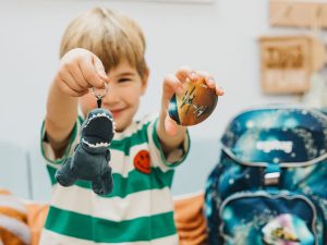 Ein Junge im Grundschulalter hält strahlend einen „Klettie“ und einen „Hangie“ von ergobag in die Kamera.